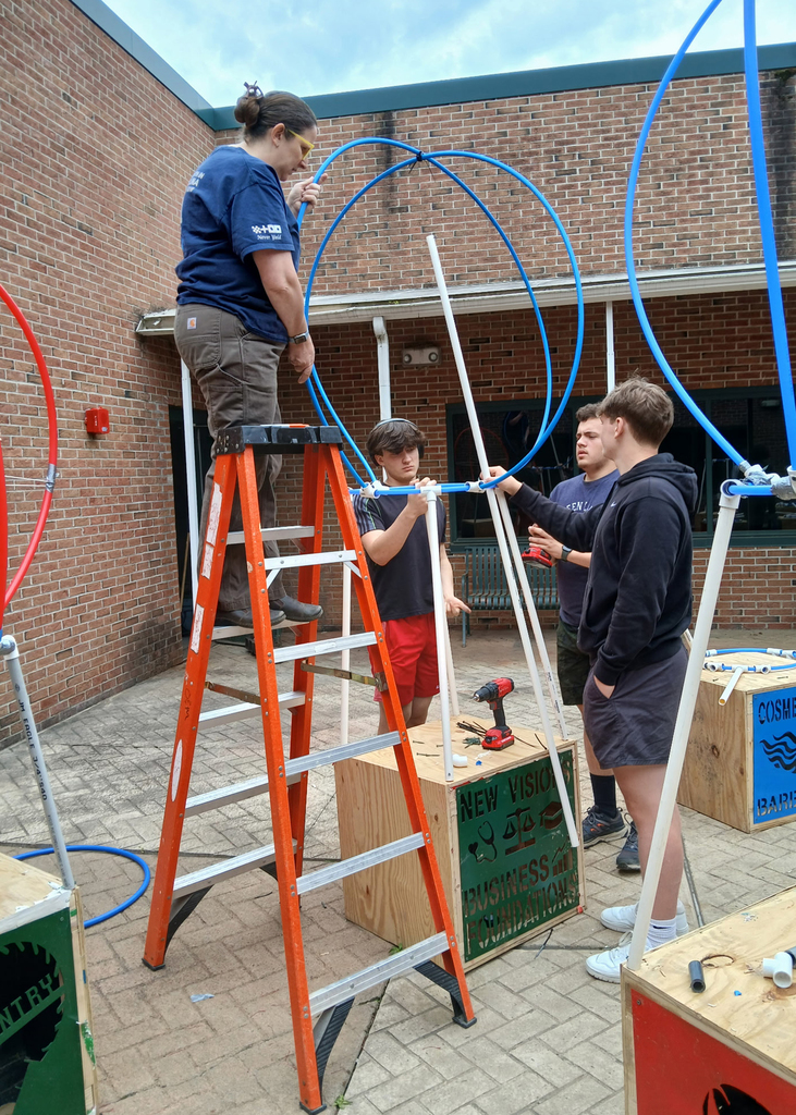 a teacher helps 2 students making a sculpture with flexible pipe