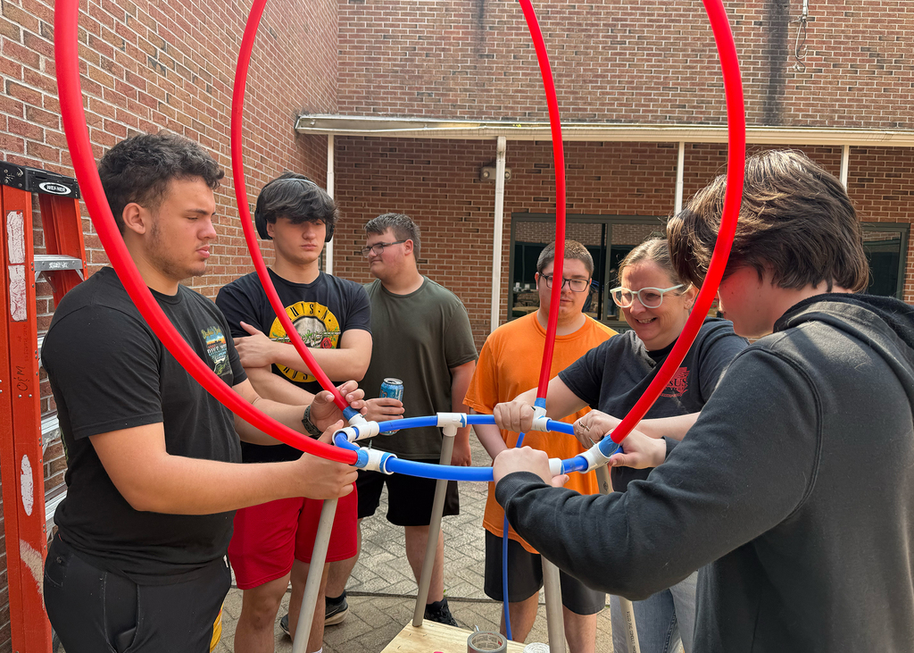 a teacher helps 2 students making a sculpture with flexible pipe