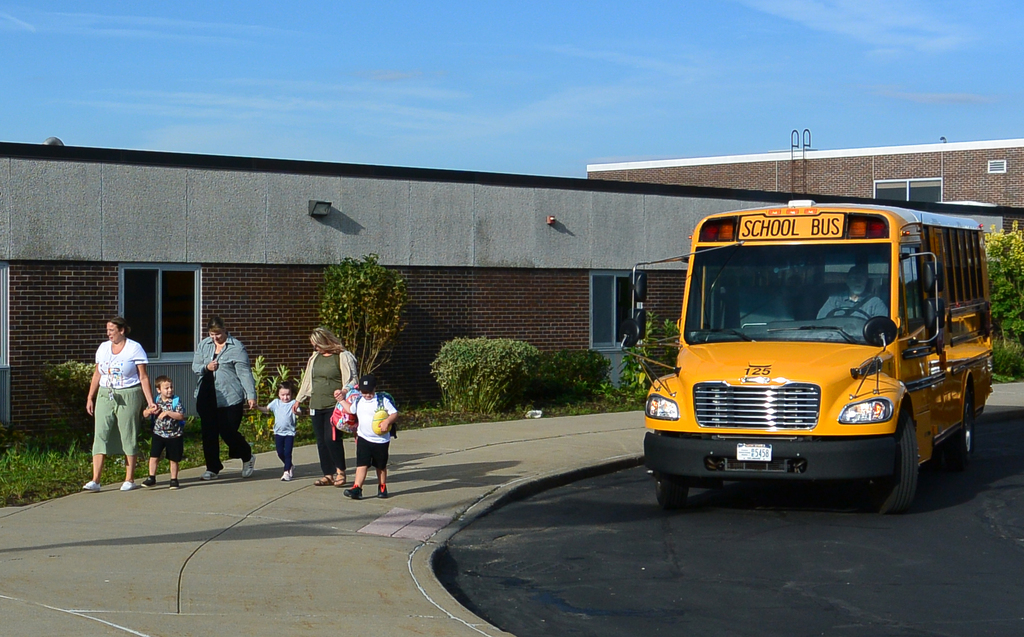 students holding hands with adults leave school bus