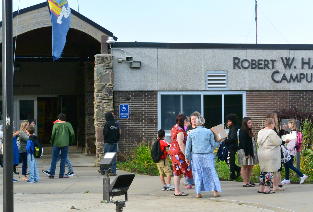students and adults mingle by buses in front of school building