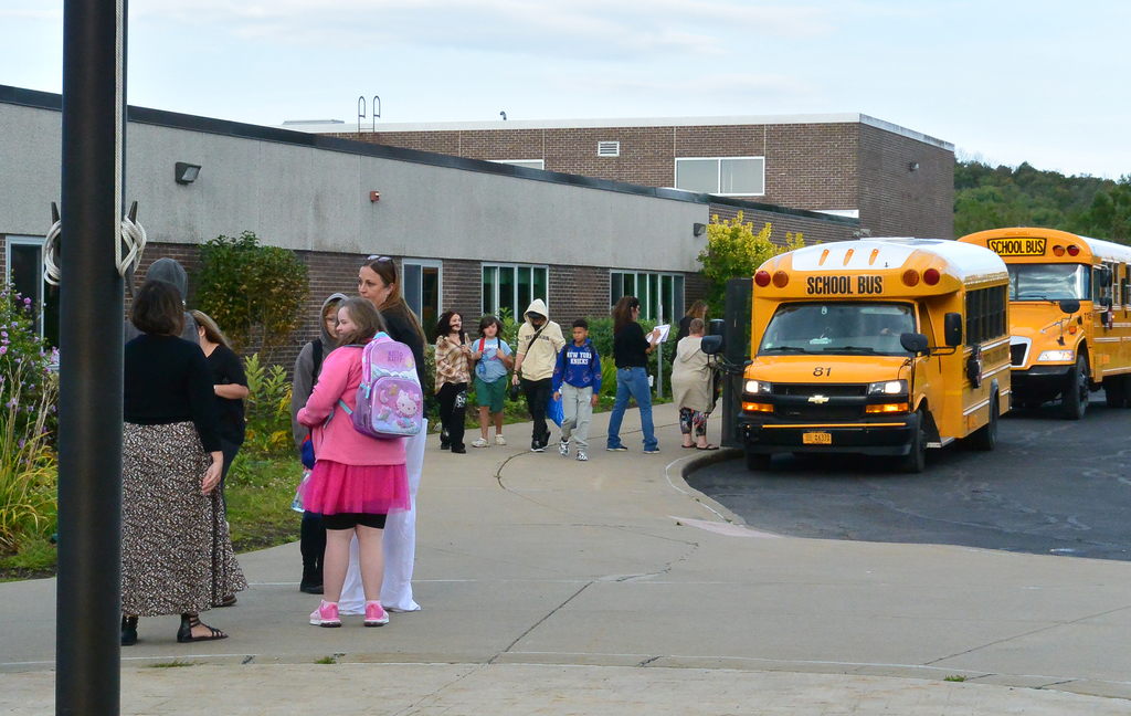 students and adults mingle by buses in front of school building