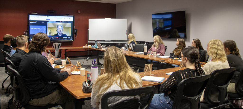 students and adult watch speaker on screen