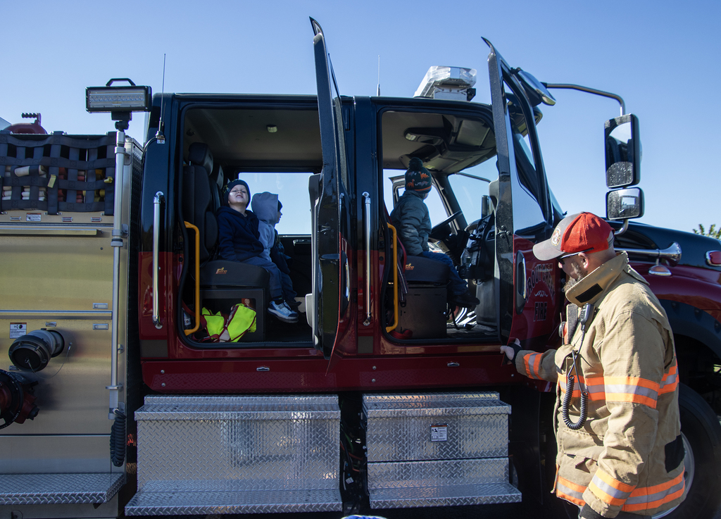 students sit in fire truck, firefighter holds door