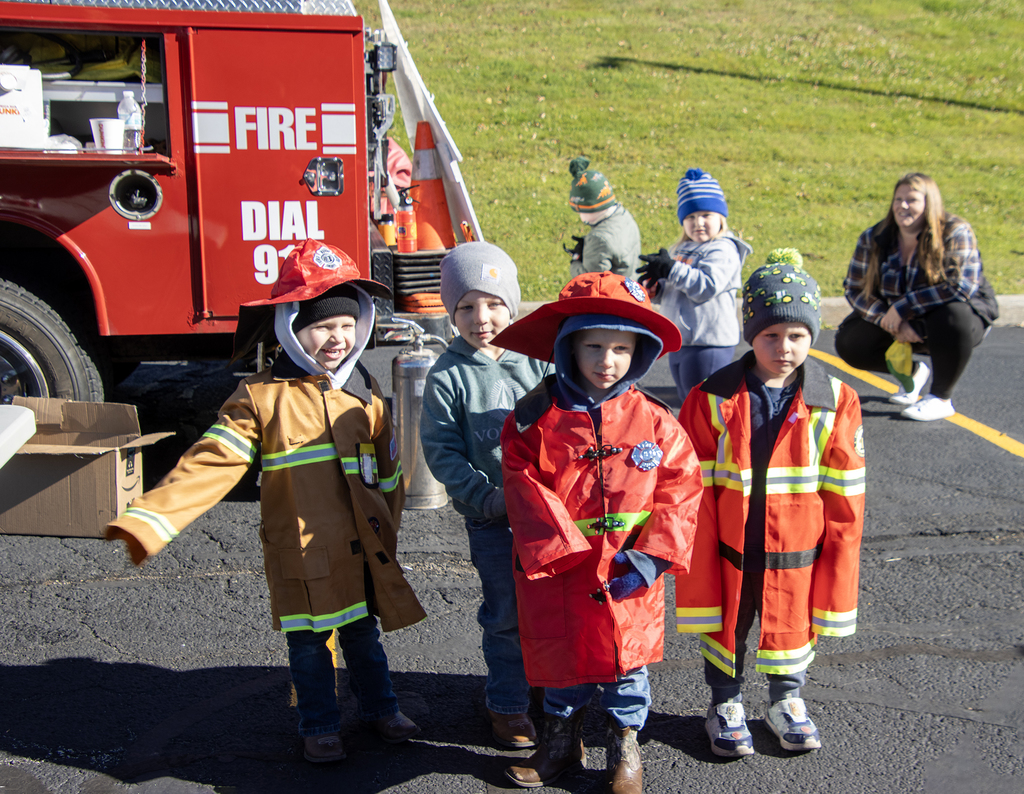 4 students try on firefighter gear, 2 other students and a teacher in background