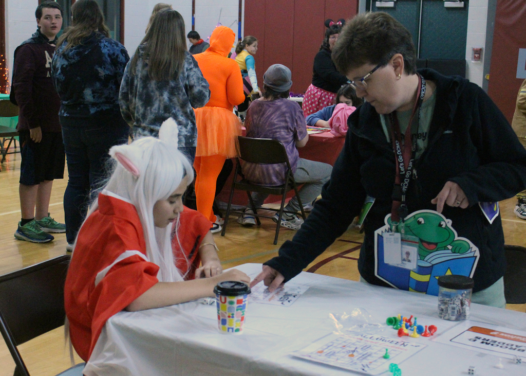student in costume at an activity table with adult on Halloween