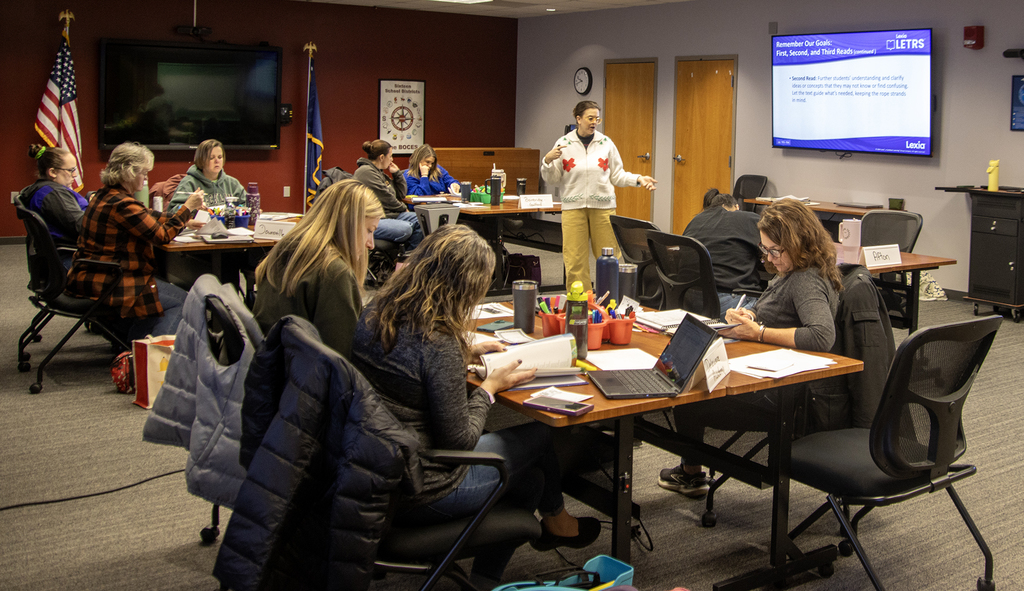 presenter speaks to group of adults around conference table in a workshop