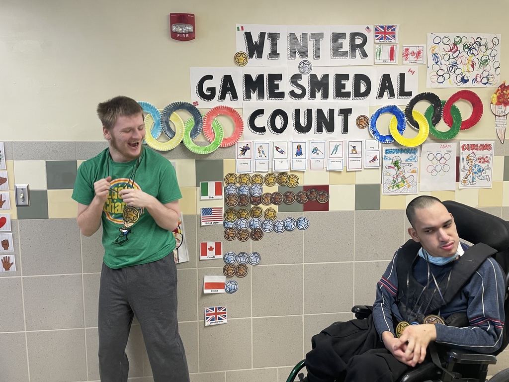 2 students smiling at Winter Olympics Medal count wall