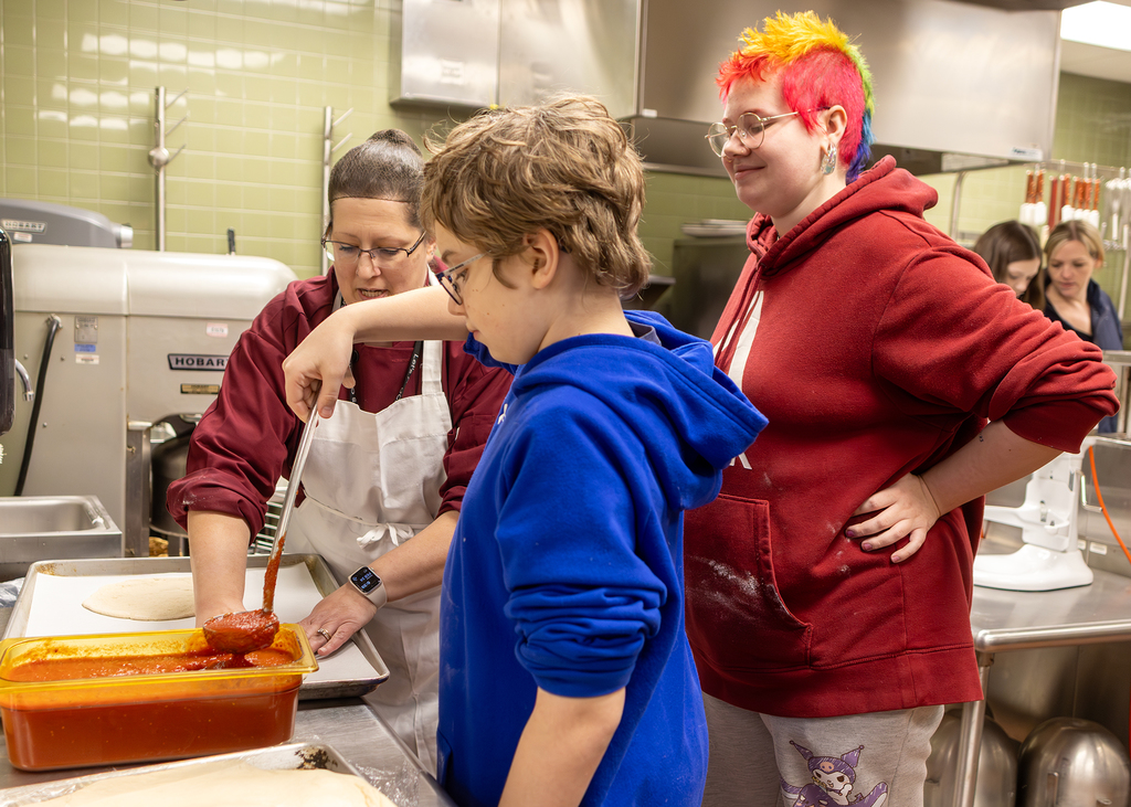 Culinary teacher supervises child ladling sauce
