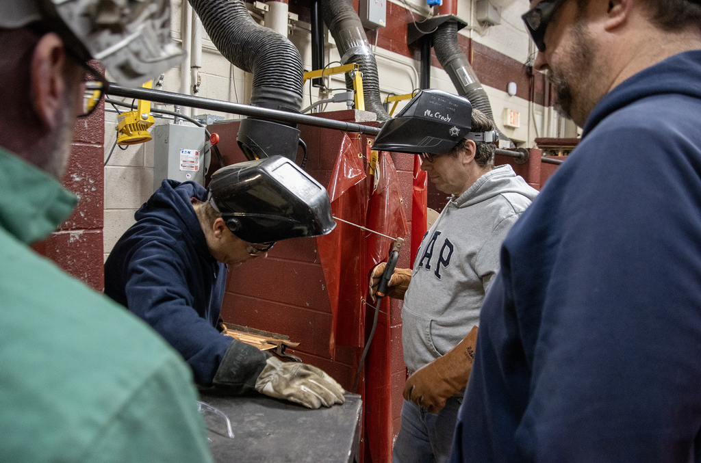 instructor speaks to three men in welding gear