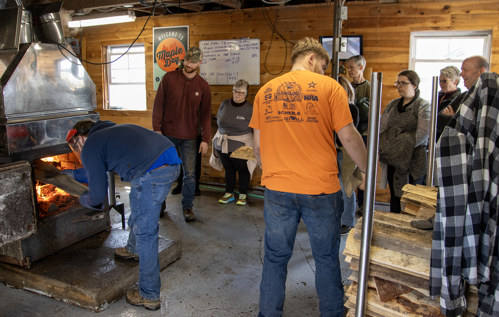 students stoke wood fire under evaporator