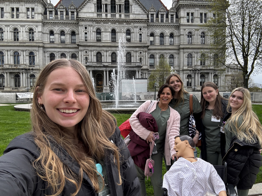 4 students, teacher and medical mannequin pose in front of state capitol