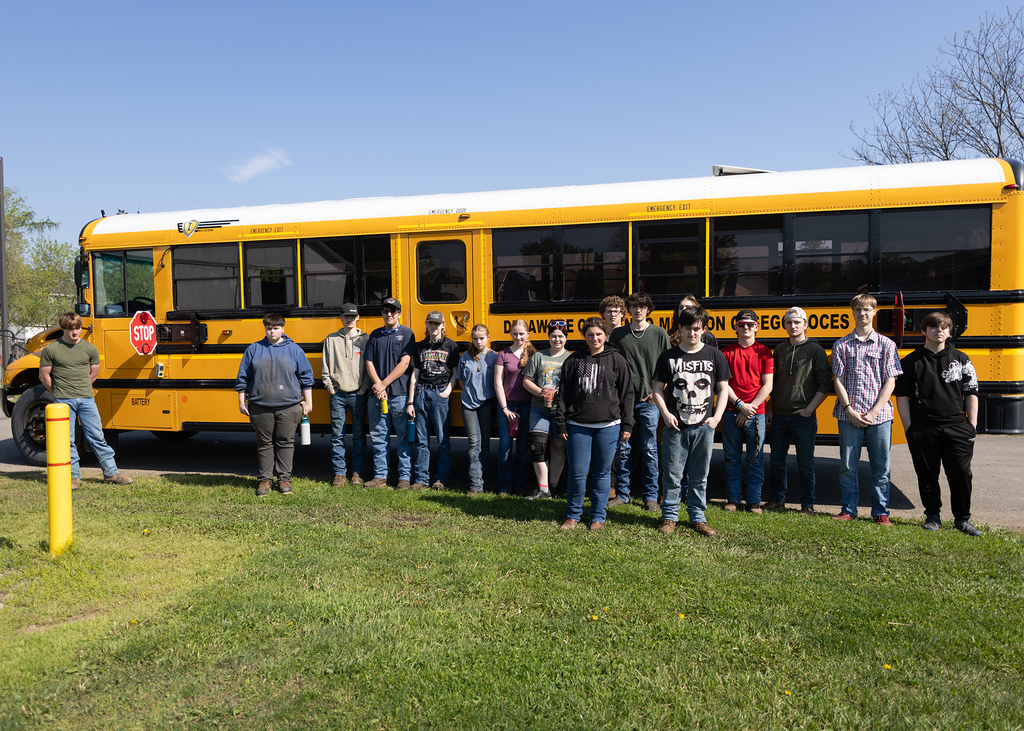 Auto tech stoduents pose in front of school bus