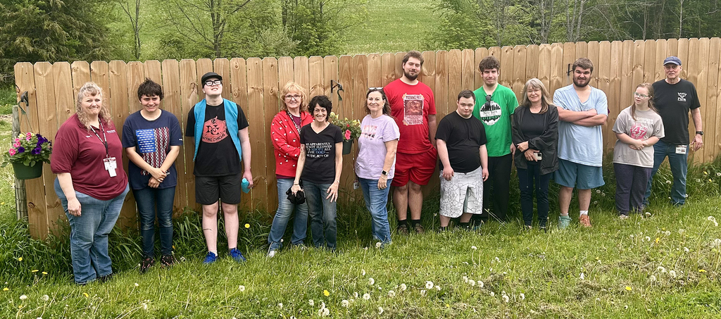 group picture of students and teachers in front of a wooden fence