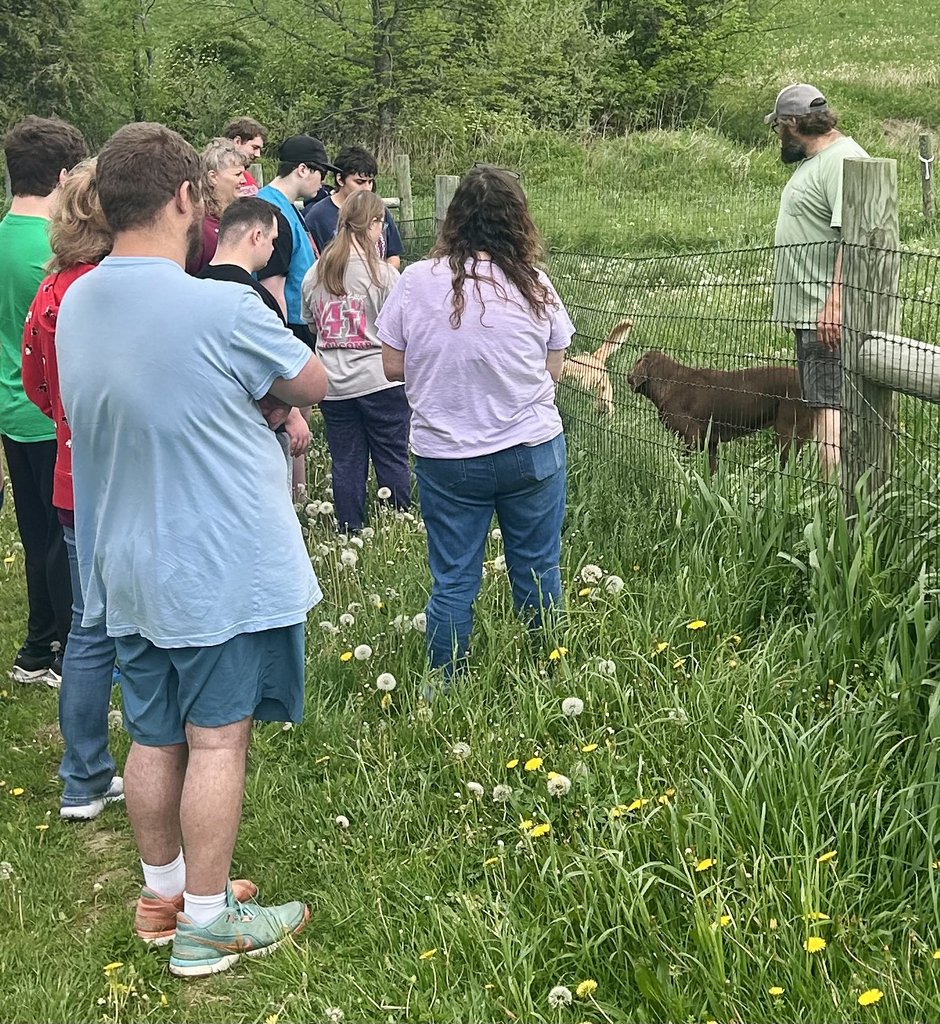 A dog handler with two dogs on one side of a fence, students and teachers on the other side