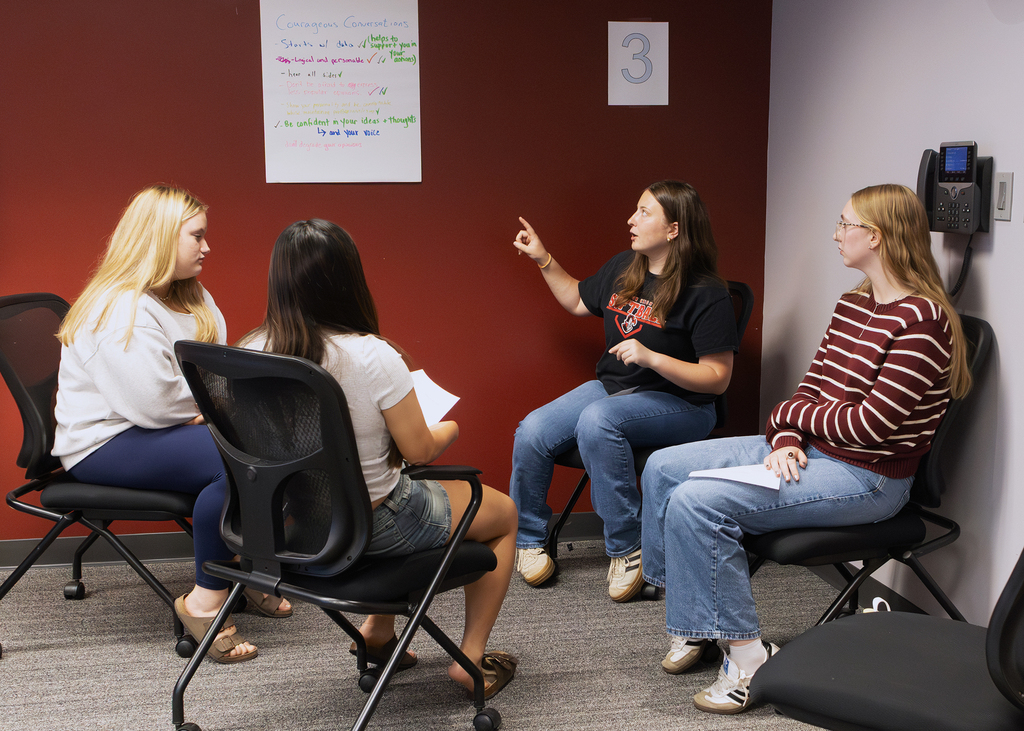 group of 4 students in a discussion, with a pad on the wall for notes