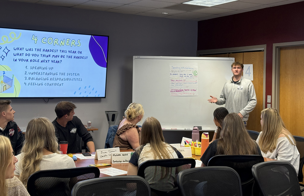 student standing and speaking before an audience, notes on the white board and on the screen