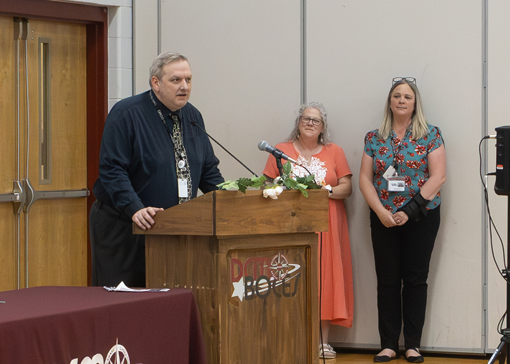Principal Ryan DeMars speaking at lectern; Jenn Lawrence and Sonnet Constable watch