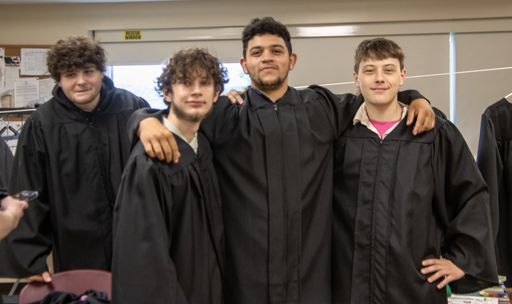 4 studewntsa pose for pictures in their graduation gowns