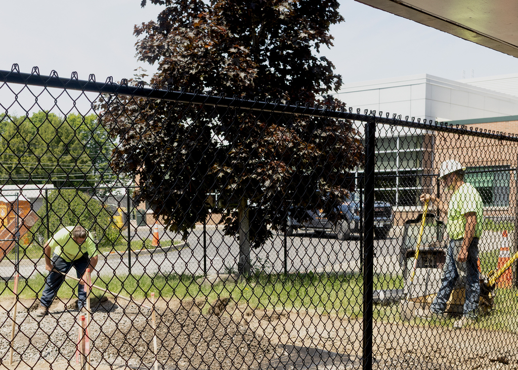 Workers using shovels behind a chain link fence
