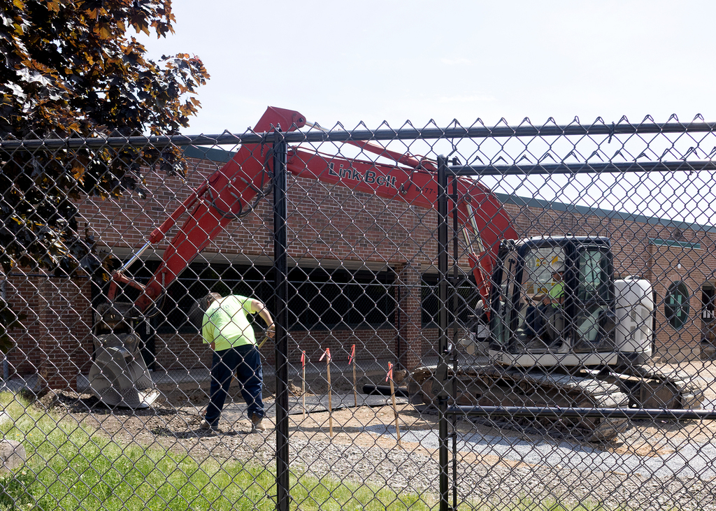 workers and an excavator at work behind the construction fence.