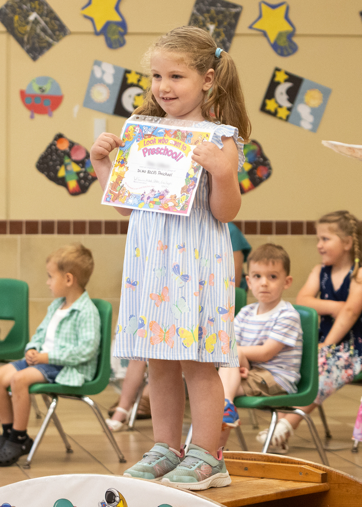 smiling child holding her preschool completion certificate