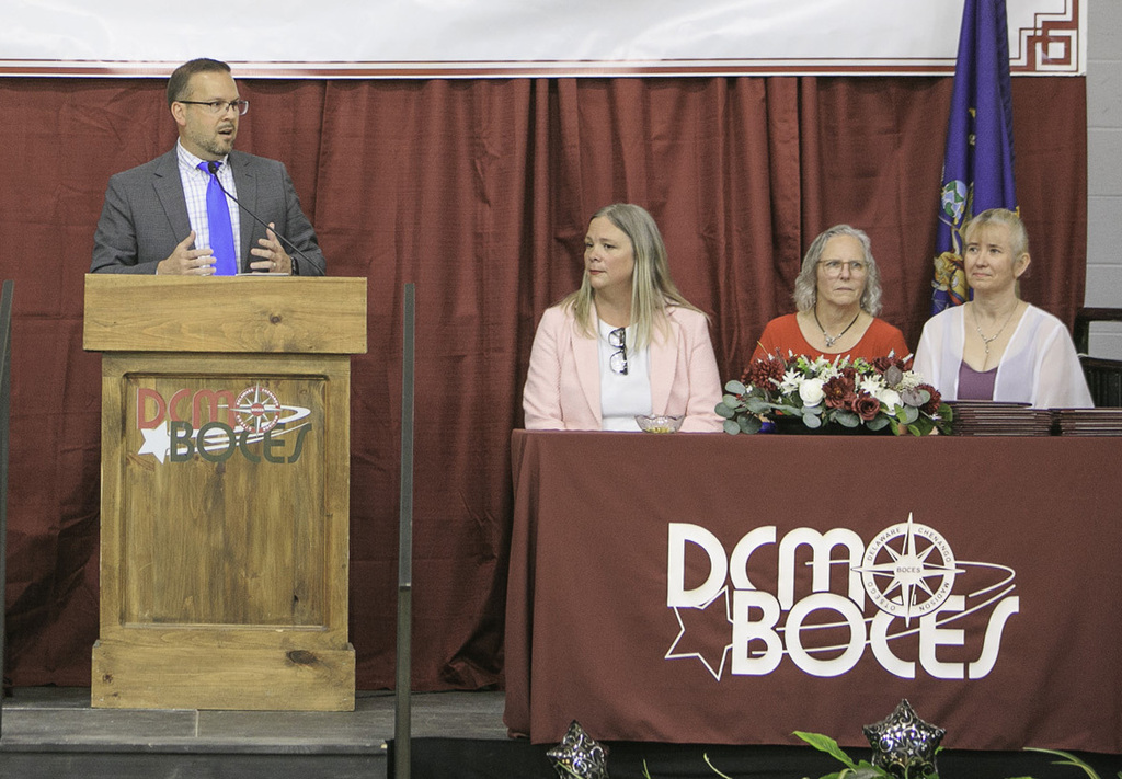 Mr. Rullo speaking at lectern, watched by three others on the stage
