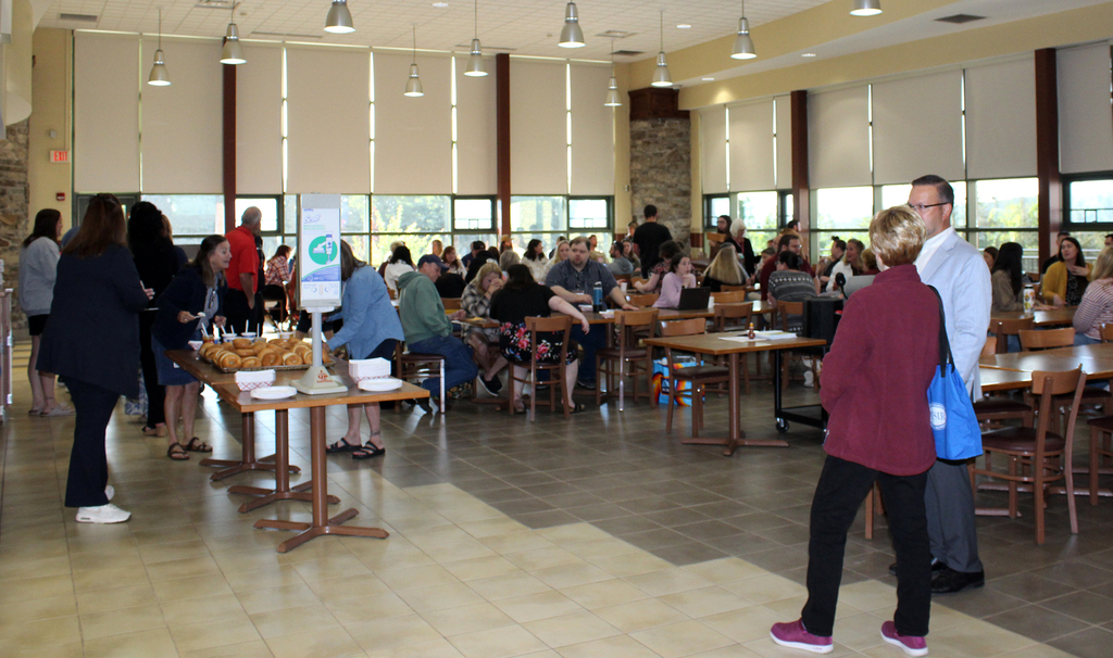 Mike Rullo and Vanessa Warren talking, employees are at tables in the cafeteria