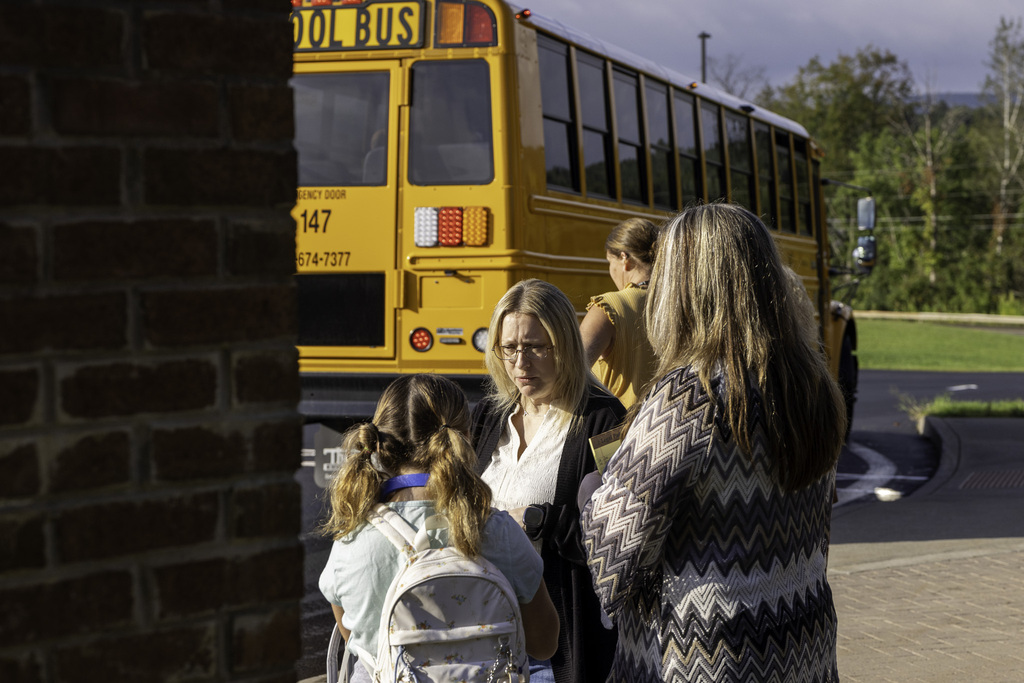 Staff talk to a student on sidewalk; school bus in background