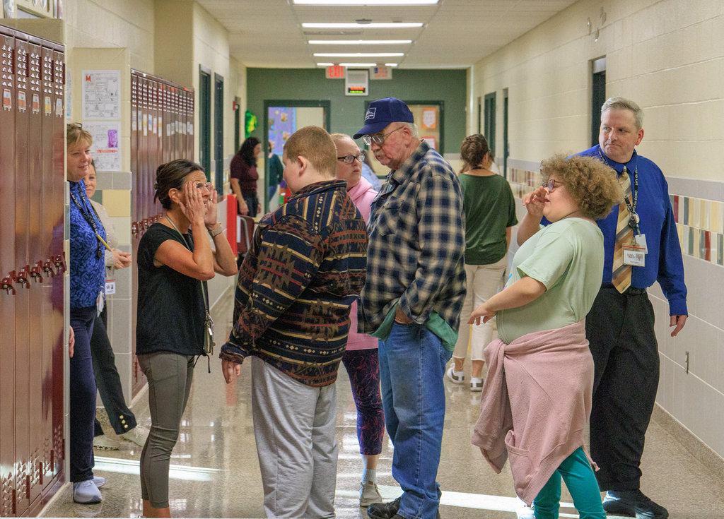 a teacher talks to a student in the hallway, student's family is also there, and the principal is walking by iin the right of the photo