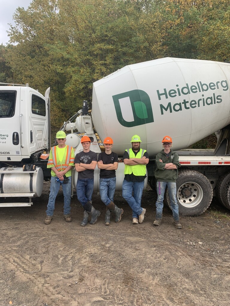 3 students and two adults in construction gear standing in front of a Heidelberg Materials cement truck