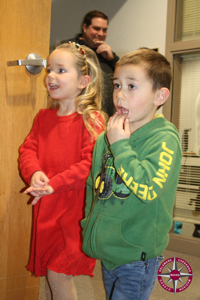 photo of two children reacting with glee to something; adult smiling in the background