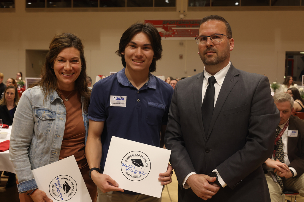student poses with 2 adults