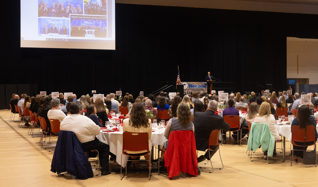 tables full of poeple in ballroom, speaker on stage