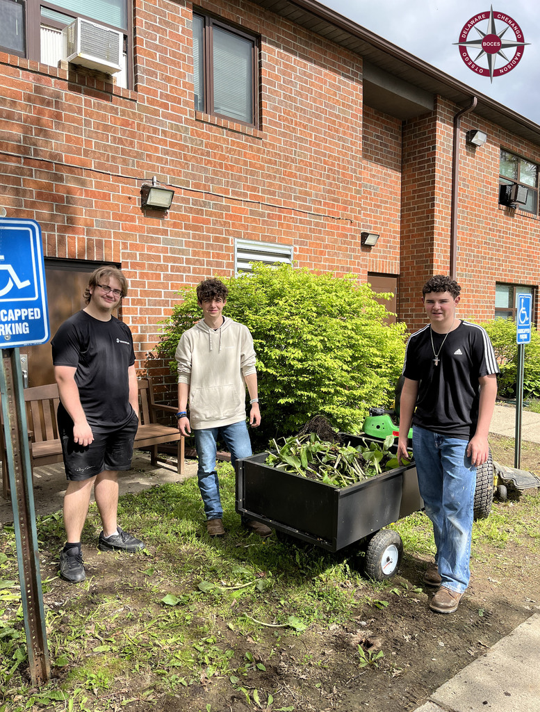 3 students pose in front of building, with yard cart and tools