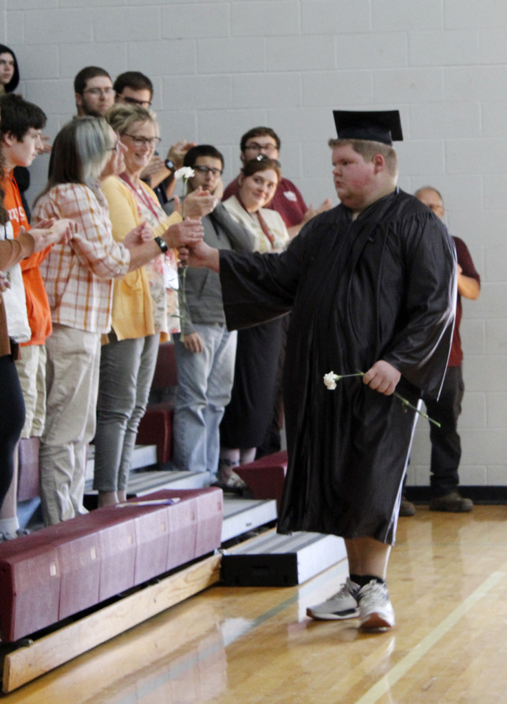 graduate hands a flower to someone in the audience