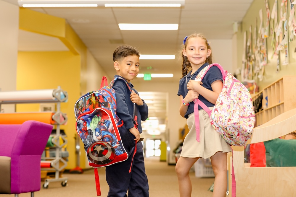 two students holding backpacks standing in the hallway