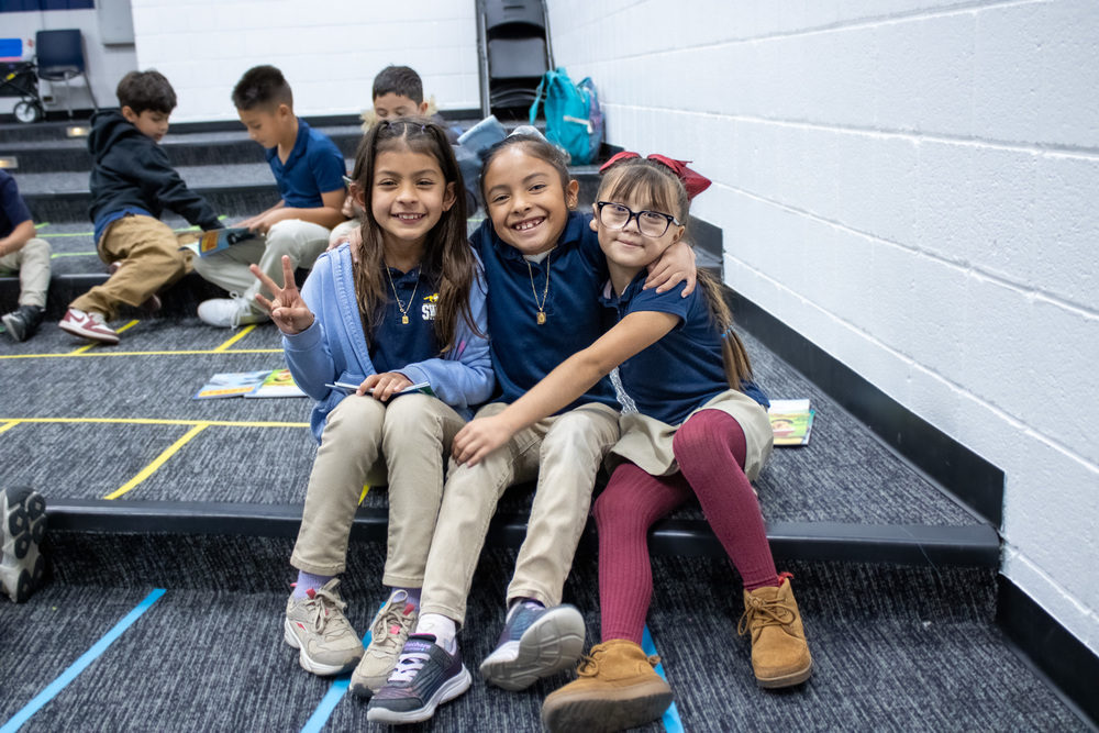 Three students hug while seated on the auditorium's stair.