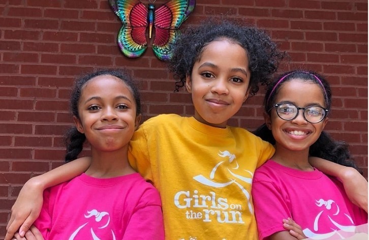 Three smiling  girls standing together wearing Girls on the Run shirts 