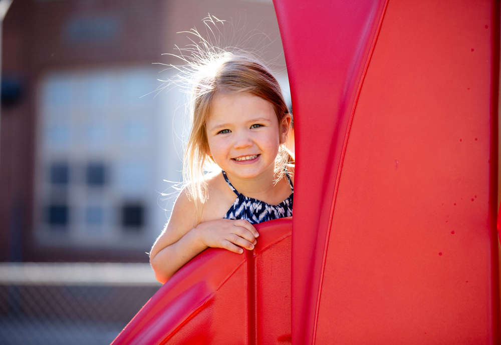 preschool student peeking around playground equipment and smiling