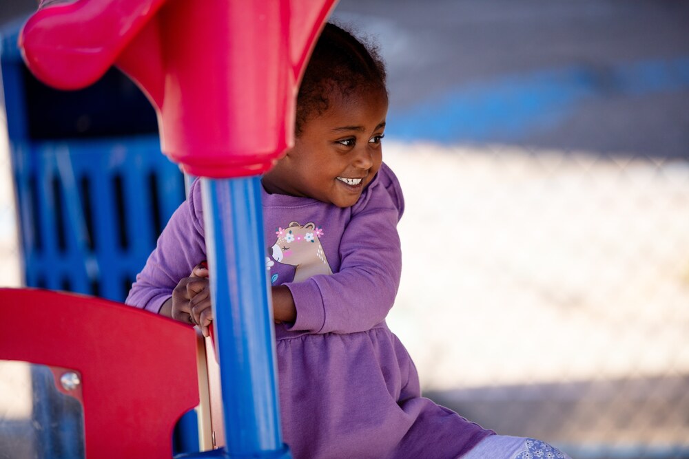 A young girl in a purple sweatshirt plays on the playground at Palmer ECE Center