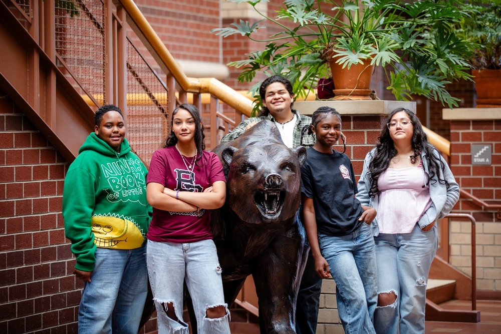 five students standing around a statue of a bear in their school