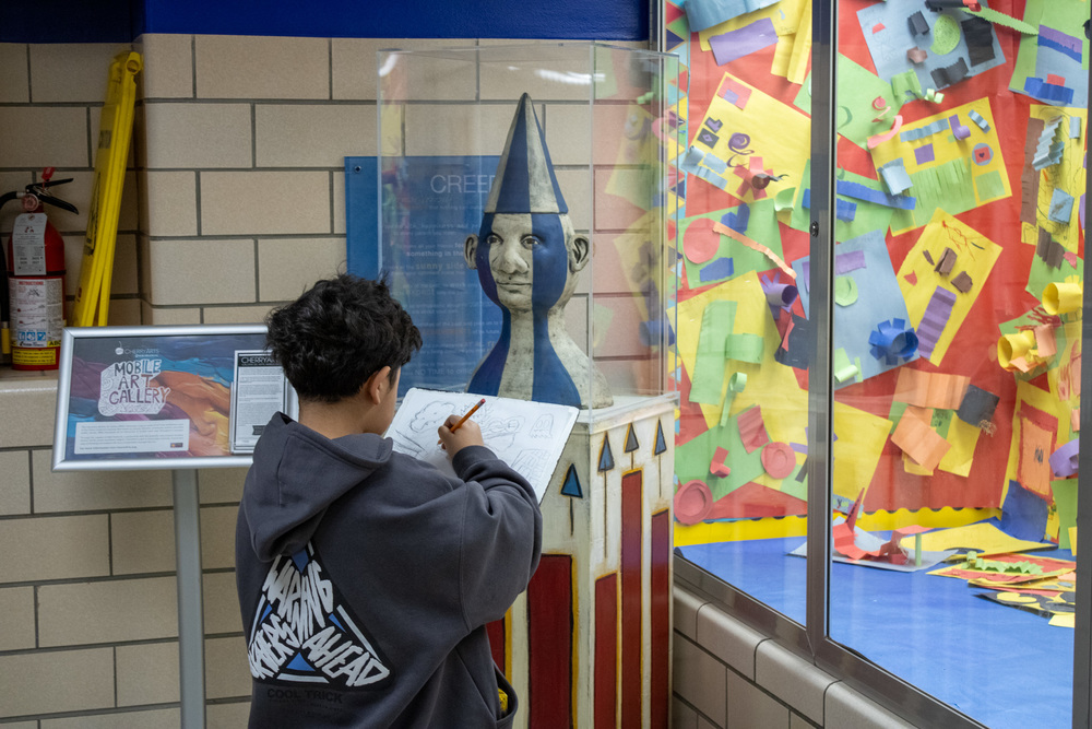 A student draws in his notebook while studying an exhibit from the Cherry Arts Mobile Gallery.