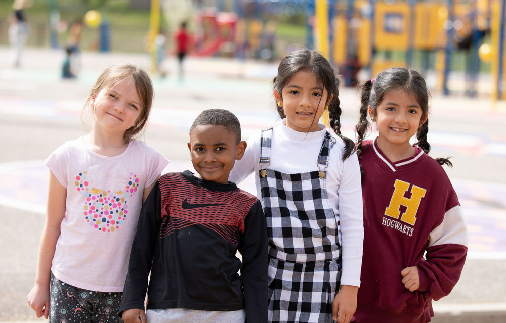 4 elementary students smiling for the camera outside in front of a playground