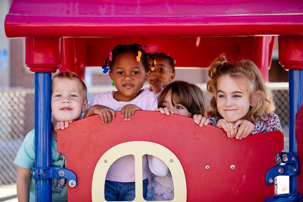 five students playing on playground equipment and smiling