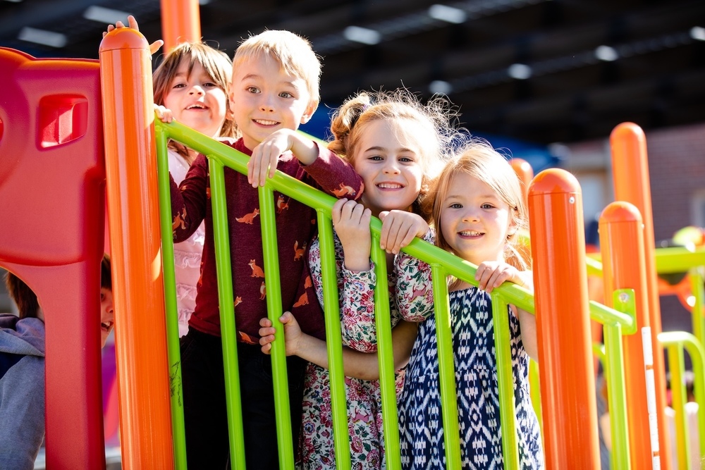 four students smiling on playground equipment