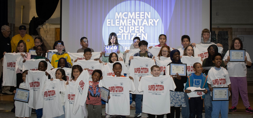 McMeen students hold up super citizen shirts and smile onstage