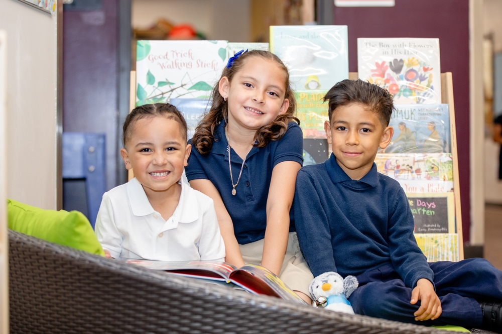 three students smiling in front of classroom library