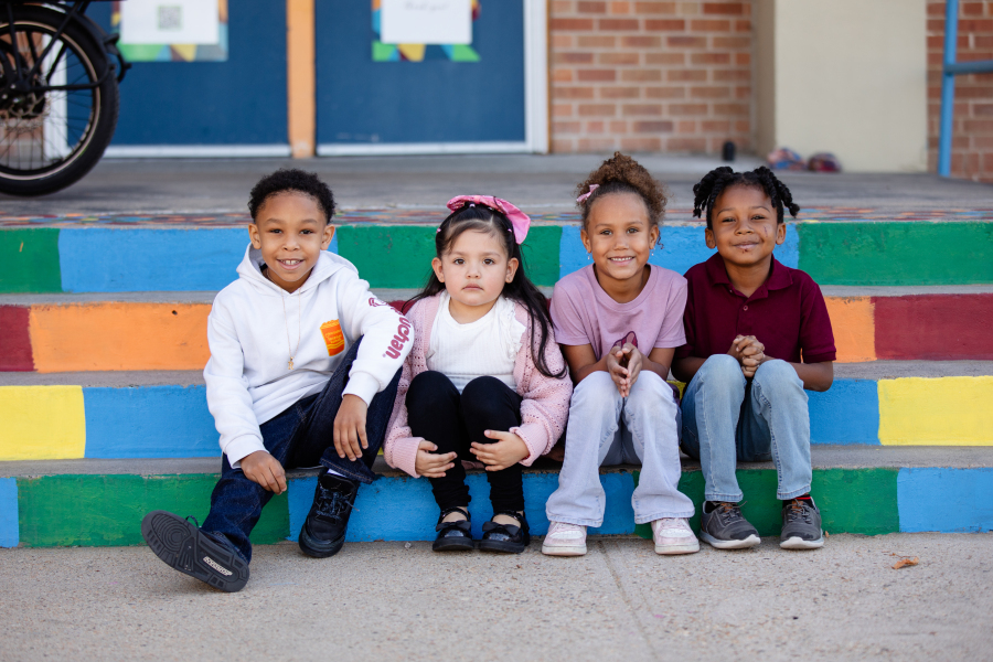 4 students sit on colorful steps and smile at the camera