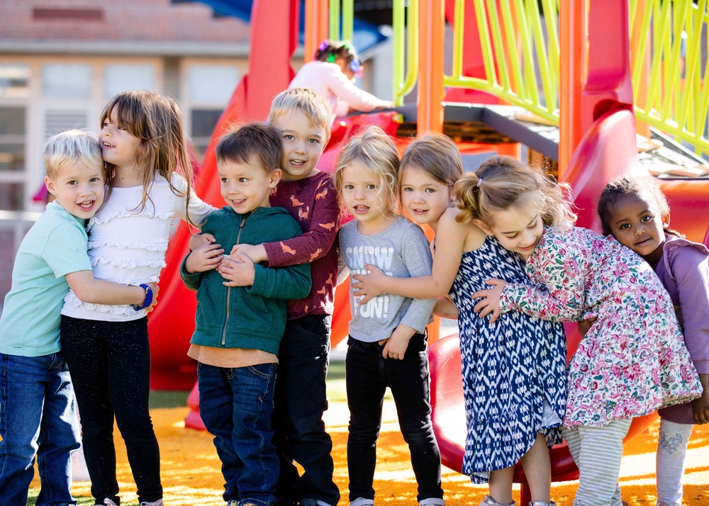 group of preschool students hugging and smiling on the playground