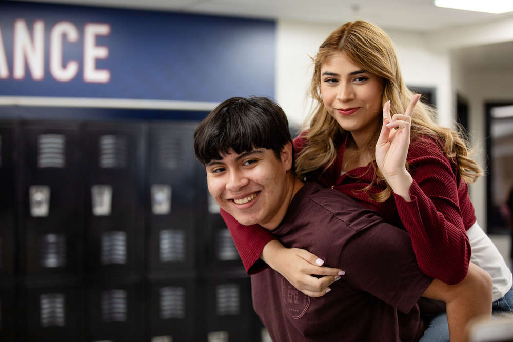Two highschoolers smiling at camera, one carrying the other on their back